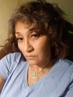 Woman with curly hair wearing a blue shirt, looking into the camera with a neutral expression.