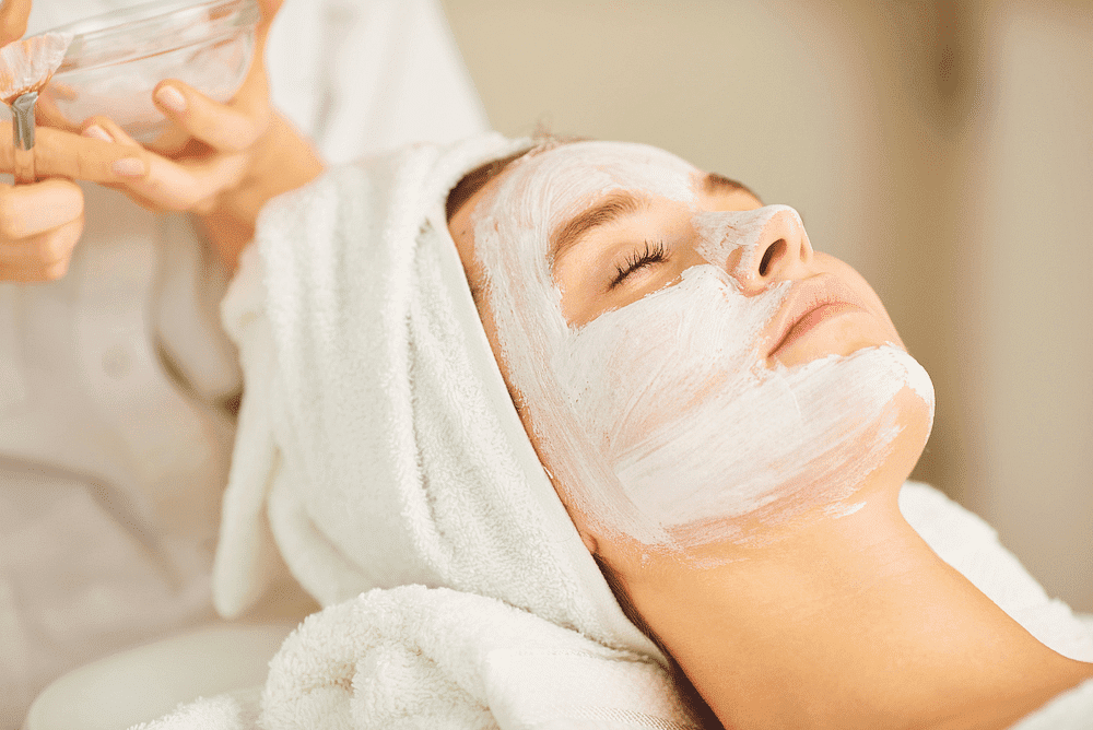 Woman receiving a relaxing facial treatment with a white mask at a spa, eyes closed, towel-wrapped hair.